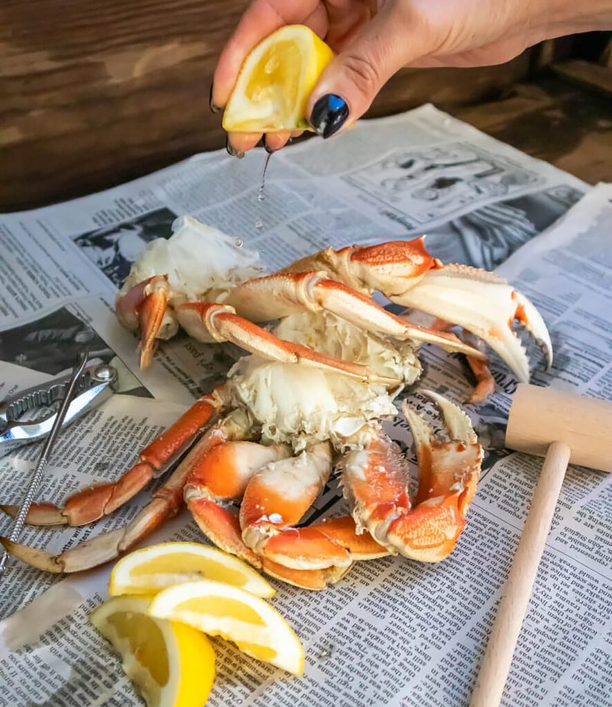 A hand squeezes a lemon slice over Dungeness crab on top of some newspaper