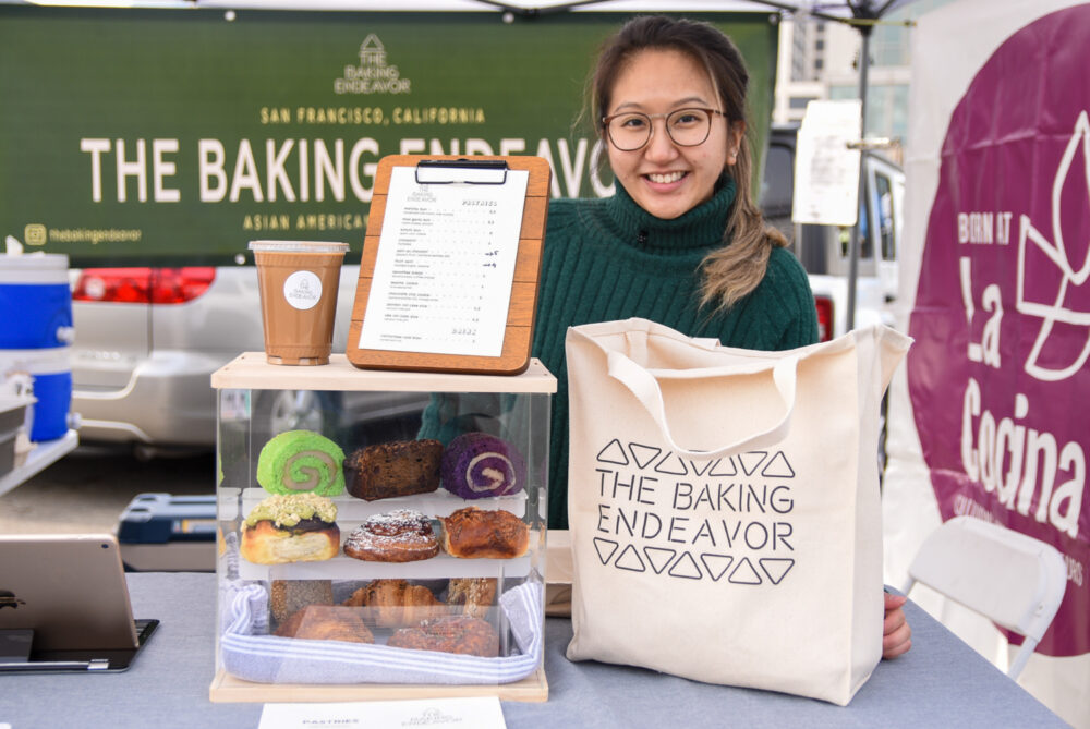Tina stands behind a display of pastries at Baking Endeavor at La Cocina's stand at the Ferry Plaza Farmers Market