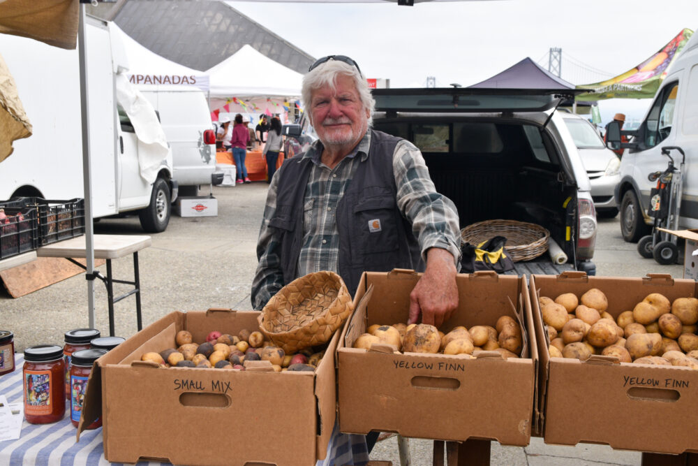 David Little sitting behind boxes of potatoes at the Ferry Plaza Farmers Market