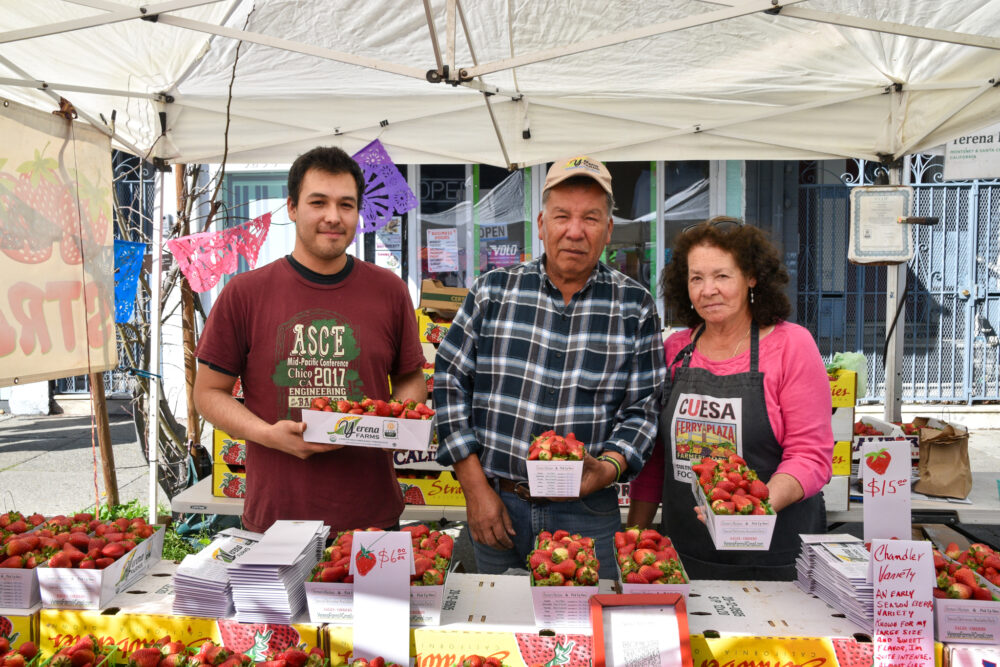 Alex, Poli, and Silvia Yerena hold strawberries at Yerena Farms' stand at Foodwise's Mission Community Market