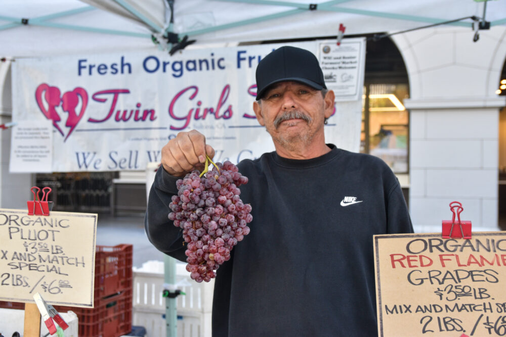Robert holding a bunch of purple grapes at Twin Girls Farm's stand at the Ferry Plaza Farmers Market