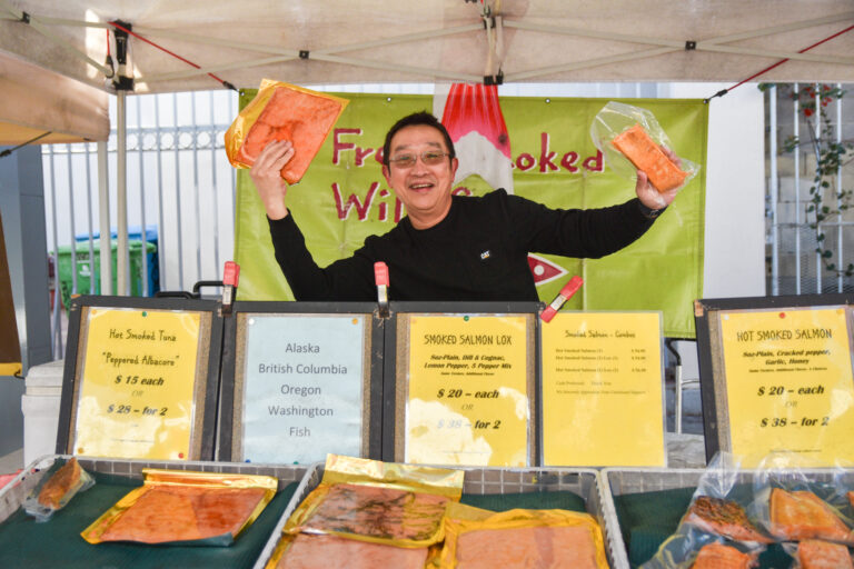 Charlie Clark holds up lox and smoked salmon at Coastside Farms and Specialties' stand at Foodwise's Mission Community Market in San Francisco.