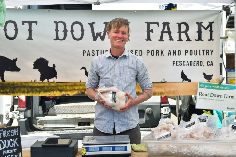 A photo of someone smiling at a farmers market stand.