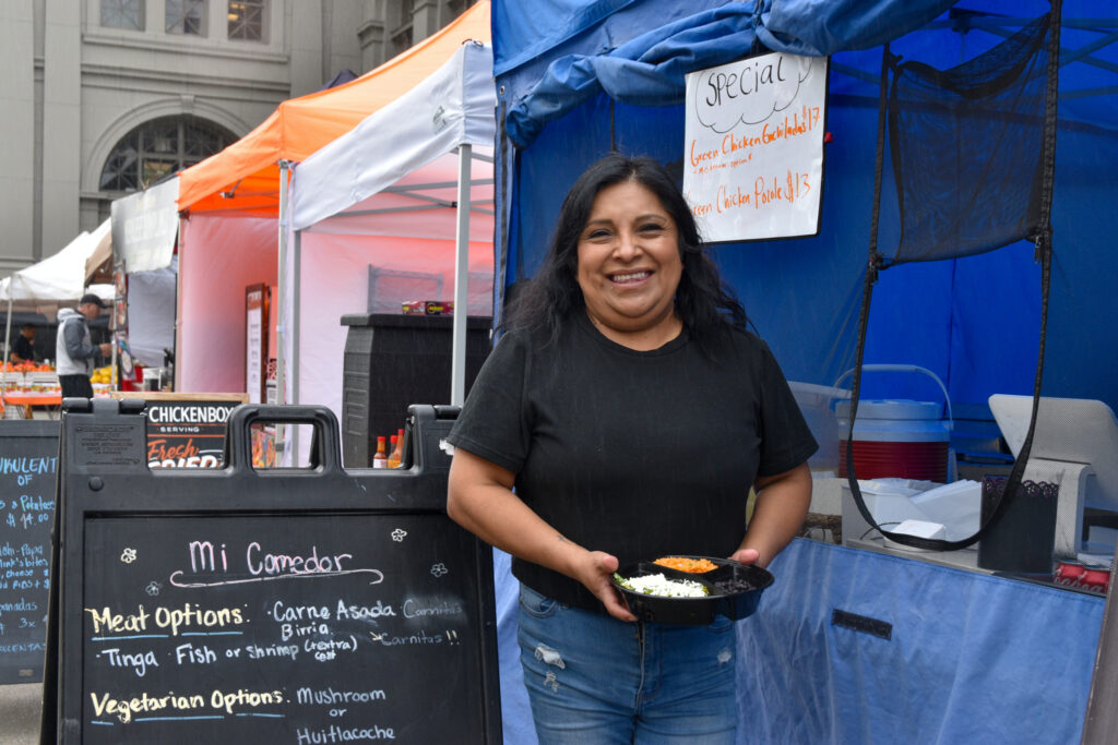 Someone poses in front of Mi Comedor's farmers market stand