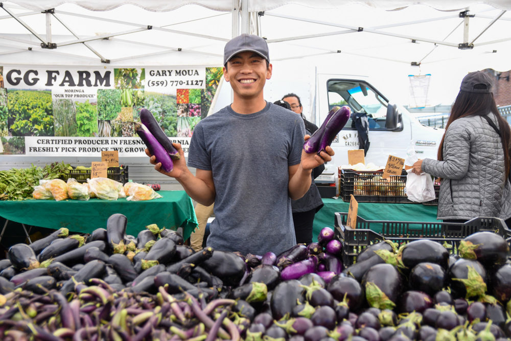 Gary Moua holding eggplants at GG Farms stand at the Ferry Plaza Farmers Market