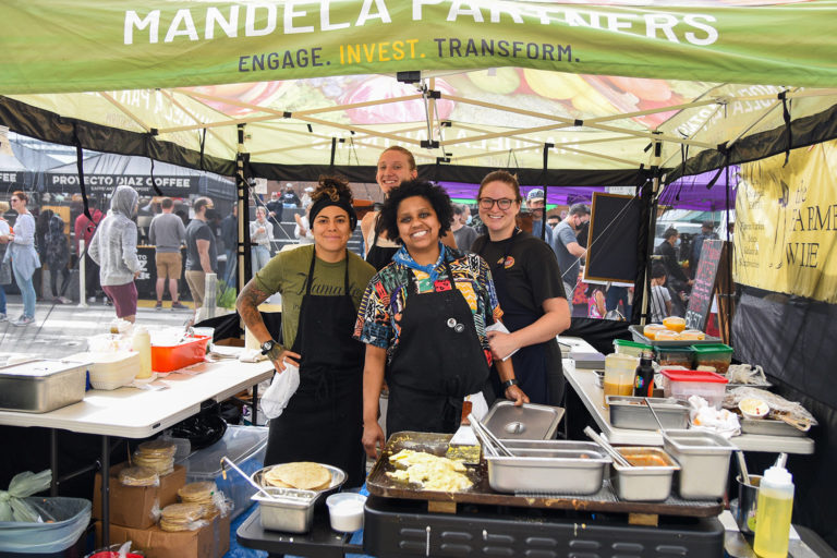 Four people, members of the LoJo's Tacos team, pose inside a Mandela Partners tent at the Ferry Plaza Farmers Market.