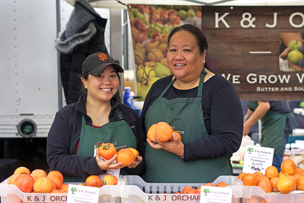 K&J Orchards booth with staff holding persimmons