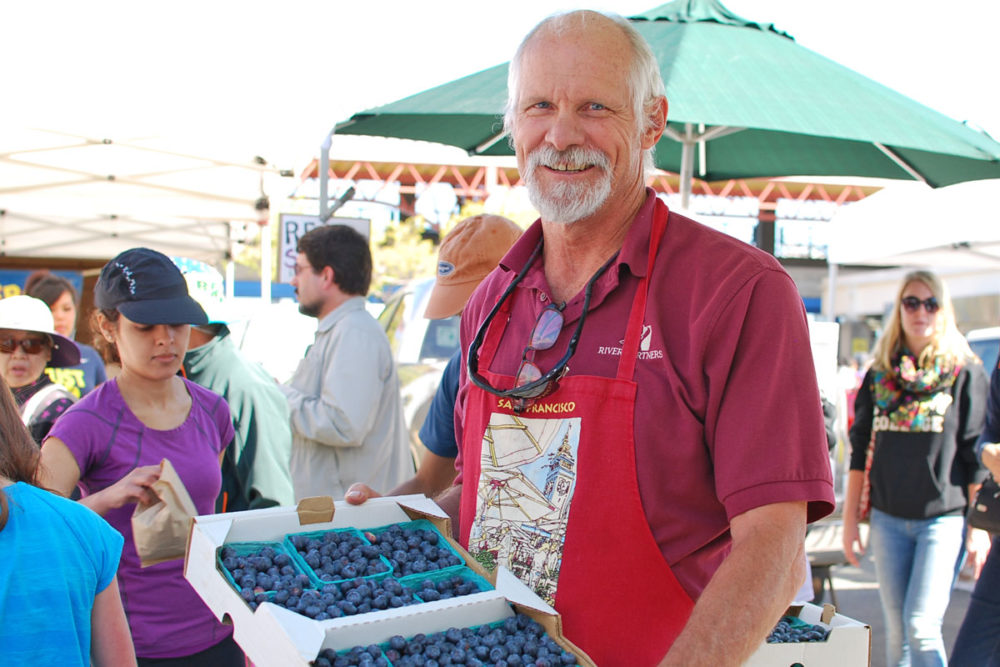 John holds a case of blueberries at Sierra Cascade Blueberry Farm's stand at the Ferry Plaza Farmers Market in San Francisco.