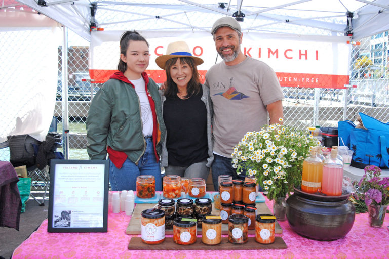 Three people, including Aruna Lee, pose at Volcano Kimchi's stand at Foodwise's Ferry Plaza Farmers Market in San Francisco.