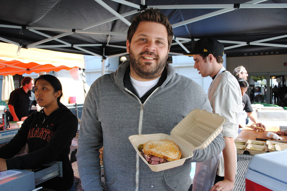Evan Bloom holds a sandwich at Wise Sons Jewish Delicatessen's stand at the Ferry Plaza Farmers Market in San Francisco.