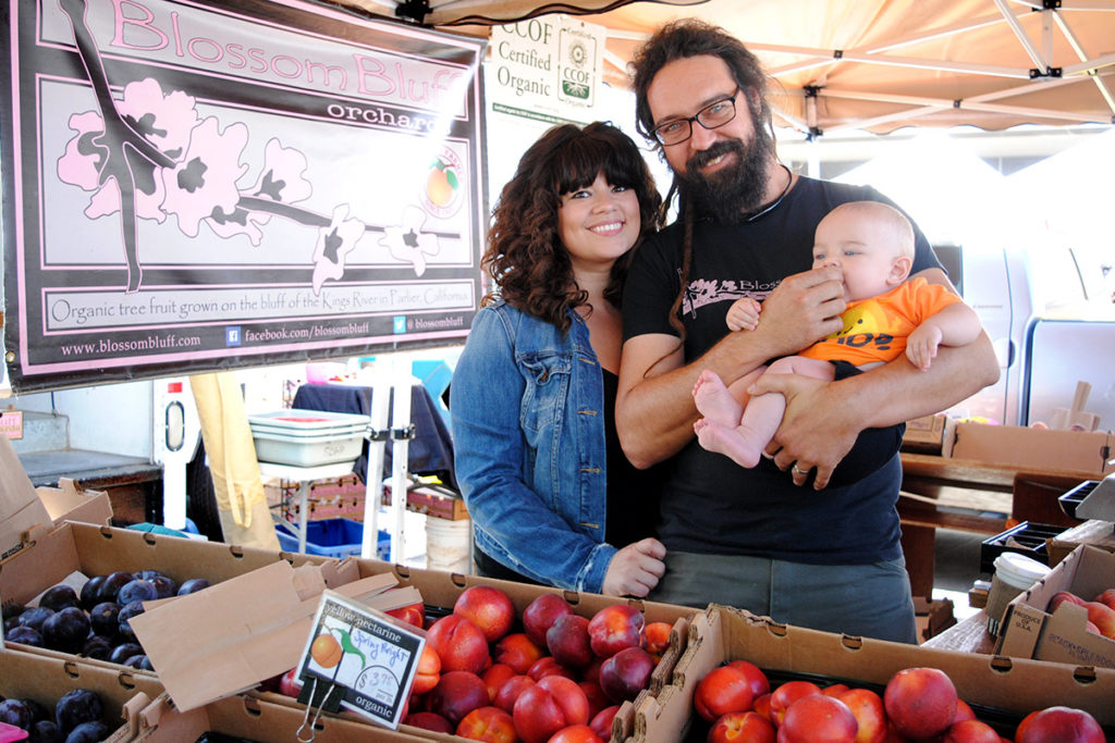 Two people hold a baby and pose at Blossom Bluff Orchards' stand at the Ferry Plaza Farmers Market in San Francicso.