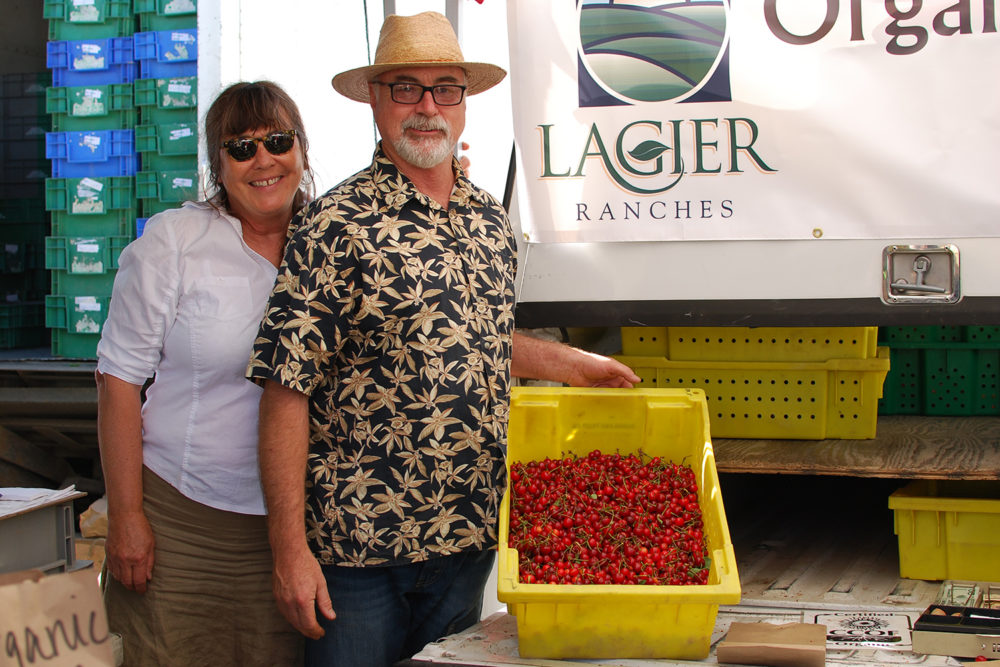 John Lagier and Casey Havre pose with a crate of red fruit at Lagier Ranches' stand at Foodwise's Ferry Plaza Farmers Market in San Francisco.