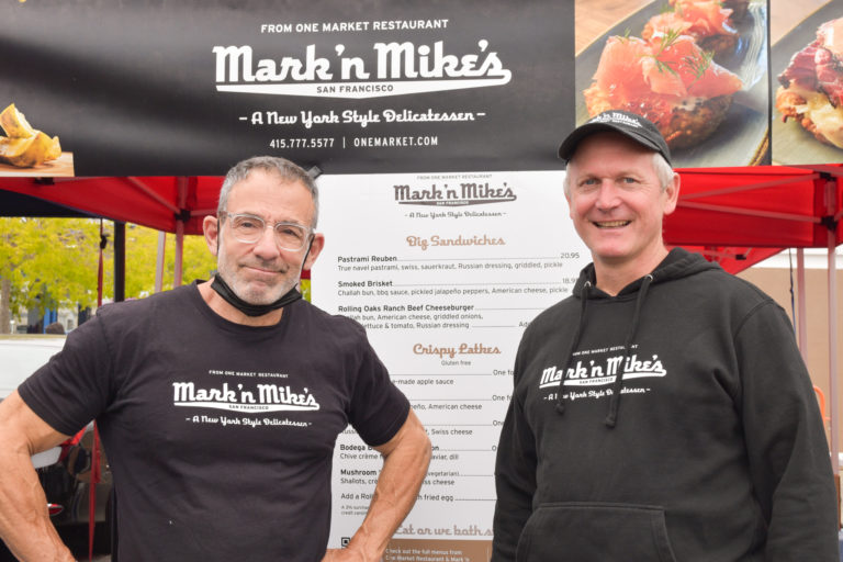 Two people pose in front of Mark 'n Mike's stand at the Ferry Plaza Farmers Market