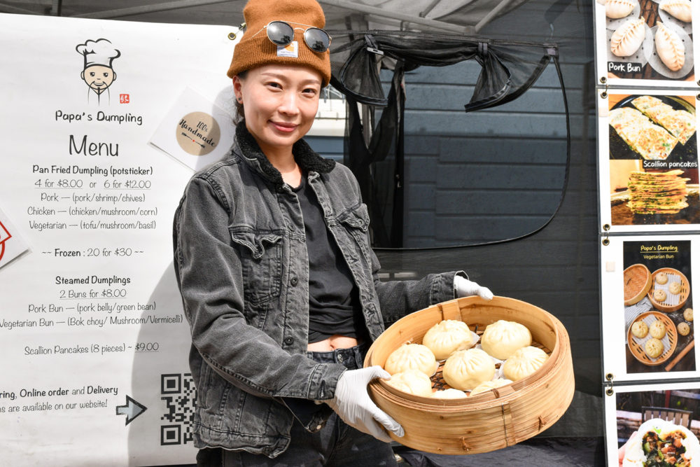Jojo Zhu holds steamed buns in front of Papa's Dumpling's stand at the Mission Community Market in San Francisco.