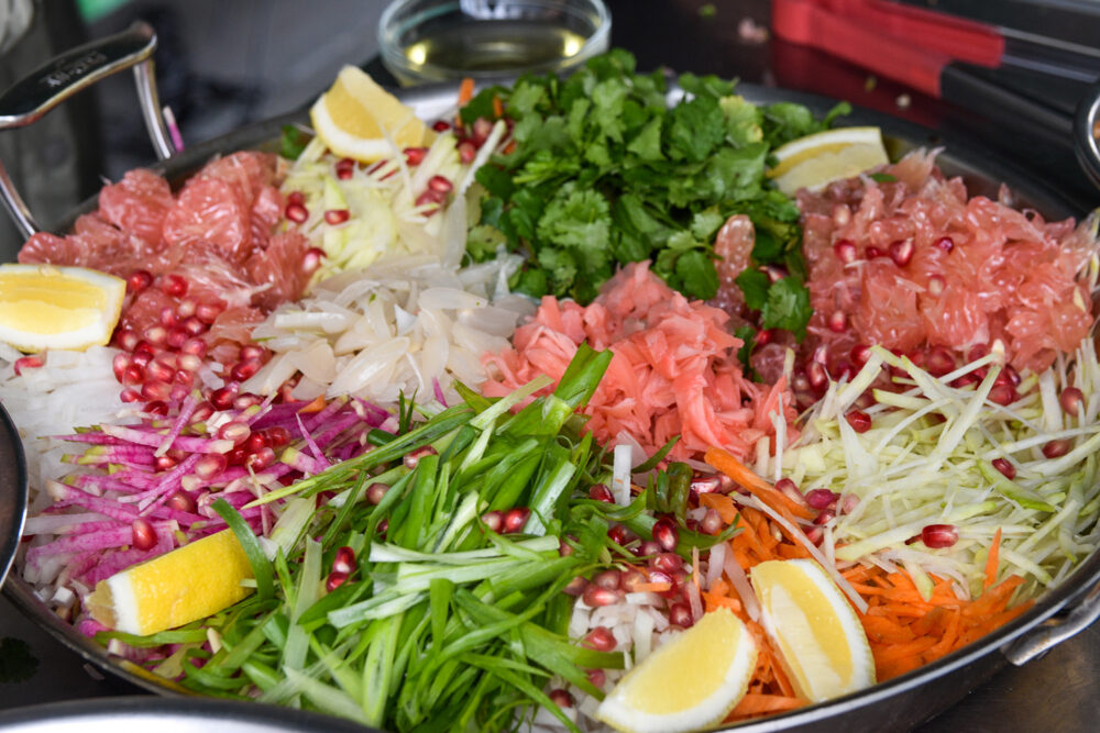 Yu Sang salad with fresh vegetables, including shredded carrots and daikon radish, topped with lemon slices and pomegranate arils