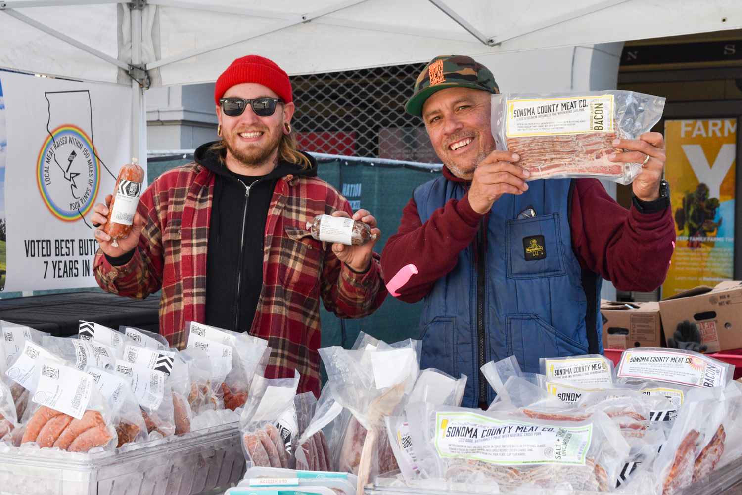 Two people pose with bacon at Sonoma County Meat Company's stand at the Ferry Plaza Farmers Market.