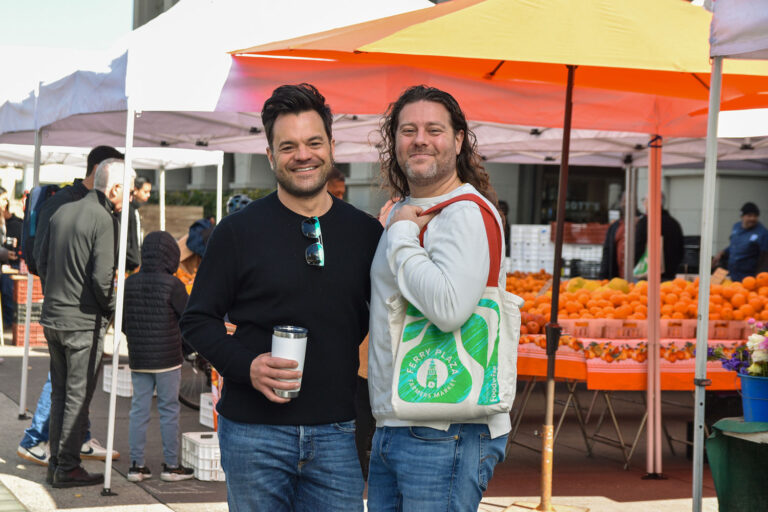 Two people pose in front of stands at the Ferry Plaza Farmers Market.
