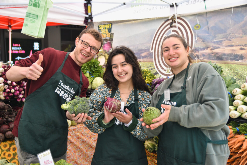 Case, Julia, and Nadia hold vegetables at the farmers market