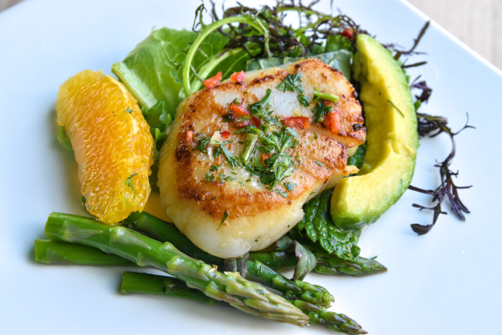 Grilled scallop on salad with an orange slice, avocado slice, and grilled asparagus