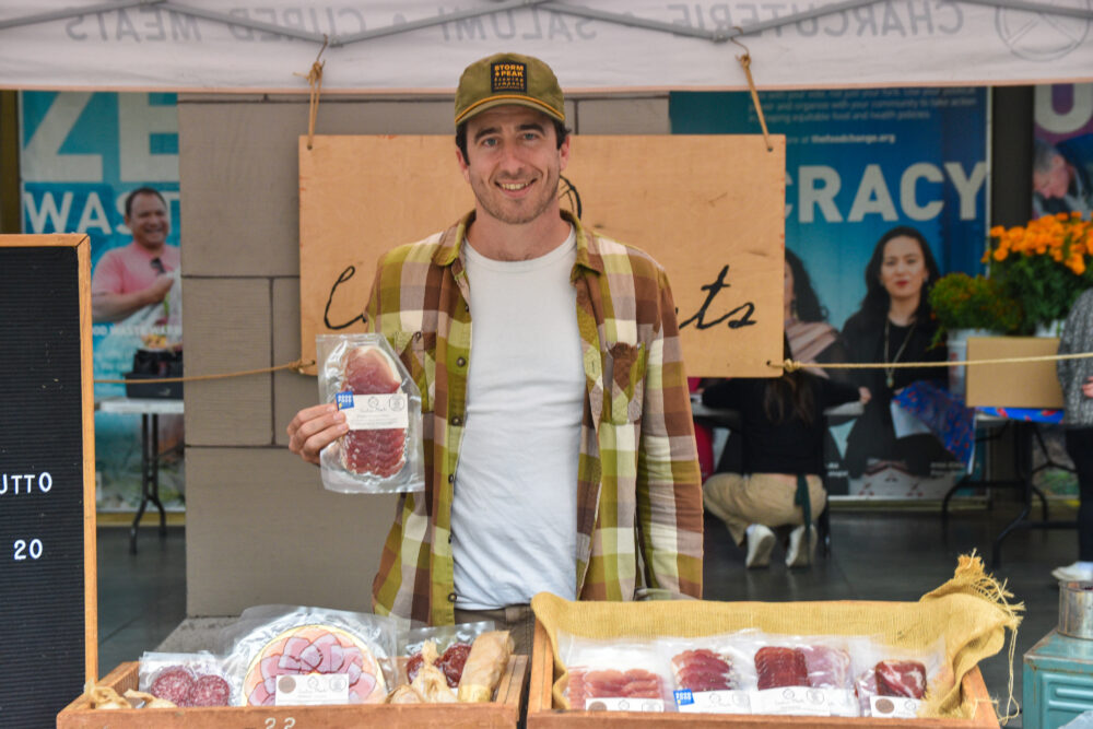 John Ginanni holding up charcuterie at Canteen Meats' stand at the Ferry Plaza Farmers Market