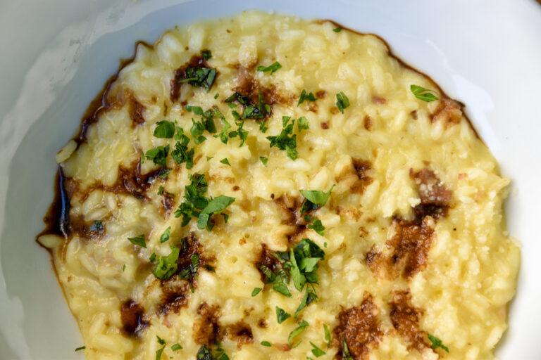 A butter yellow risotto, topped with brown vinegar and garnish, served in a white dish.