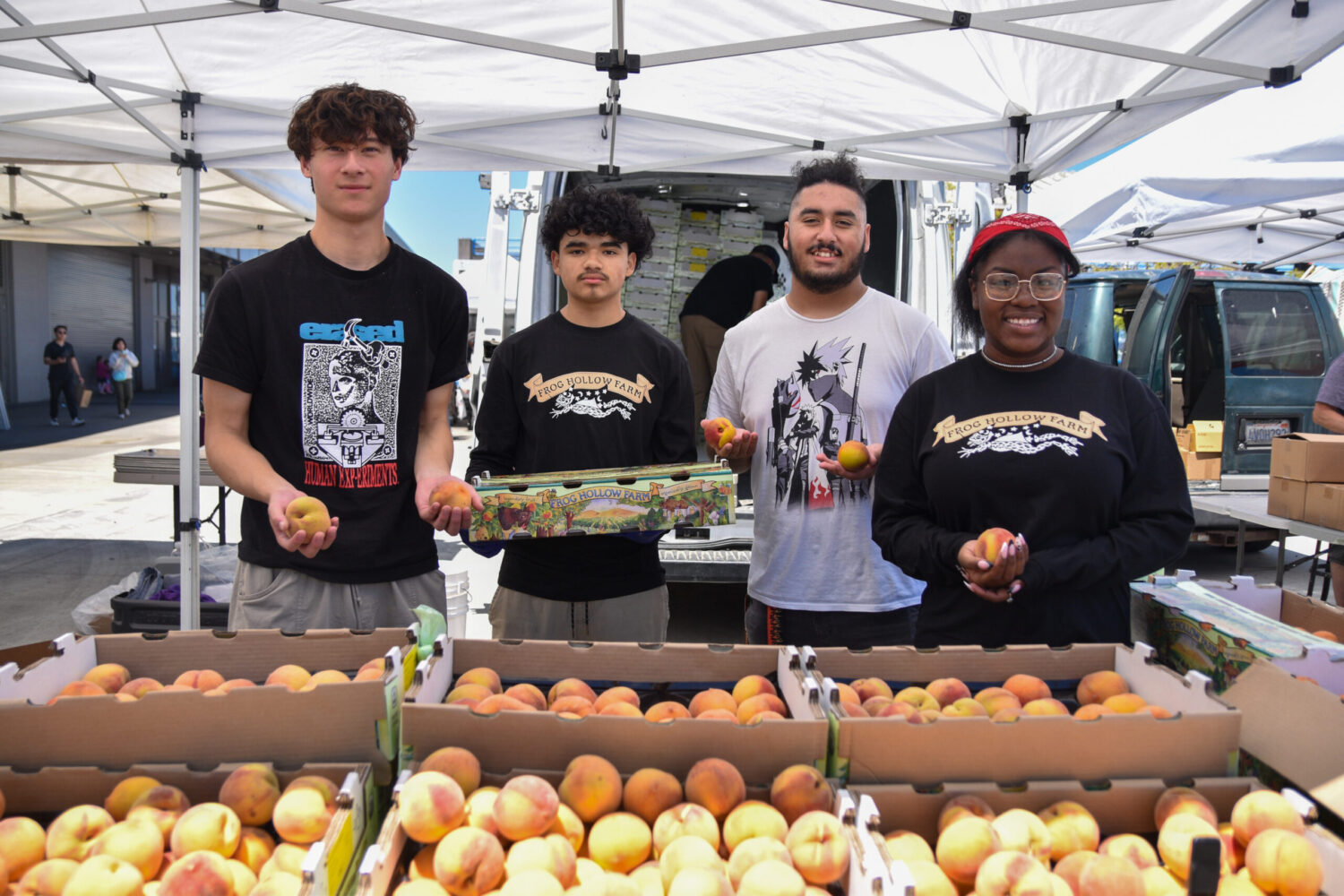 Foodwise Teens pose for a photo at Frog Hollow Farm's stand at the Ferry Plaza Farmers Market. Peaches and stone fruit are in the foreground.