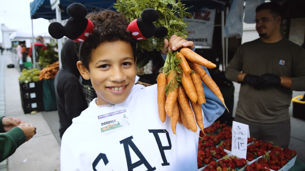 A kid holds up a bunch of carrots at the Ferry Plaza Farmers Market.