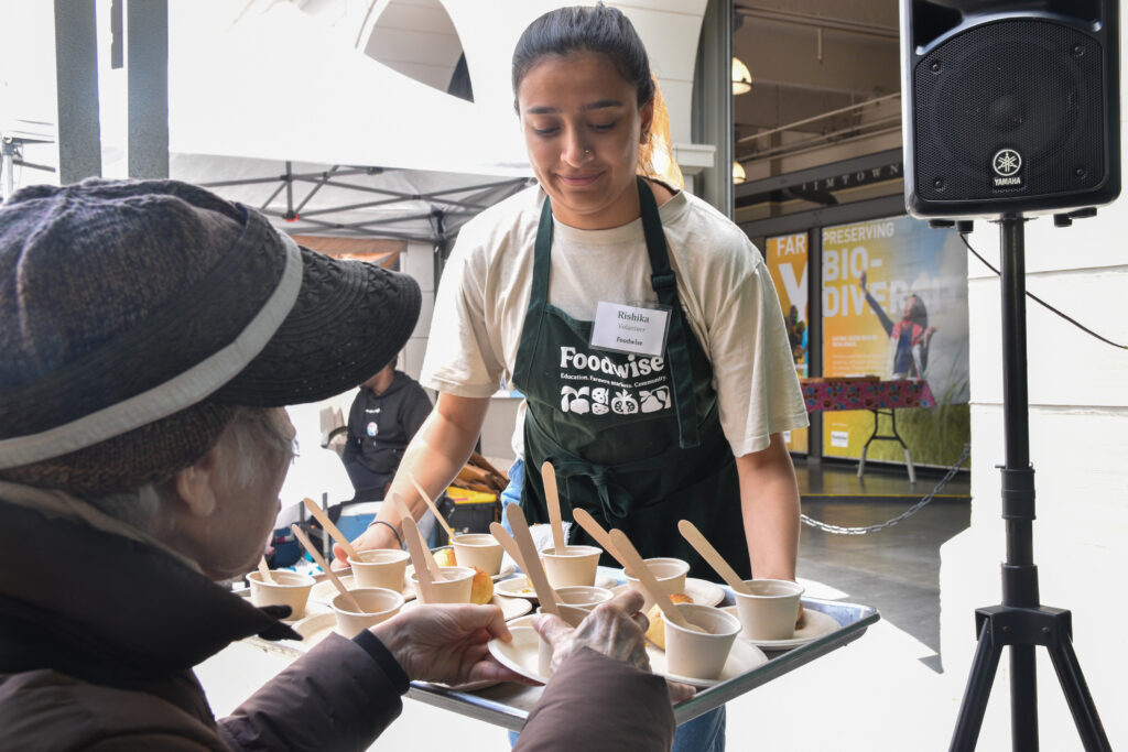 Foodwise volunteer, Rishika, passes out samples at a Foodwise demo at the Ferry Plaza Farmers Market.