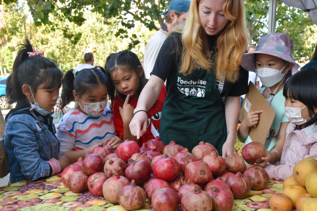 Foodwise intern Heidi Ford points out pomegranates to a group of Foodwise Kids at the Ferry Plaza Farmers Market in San Francisco.
