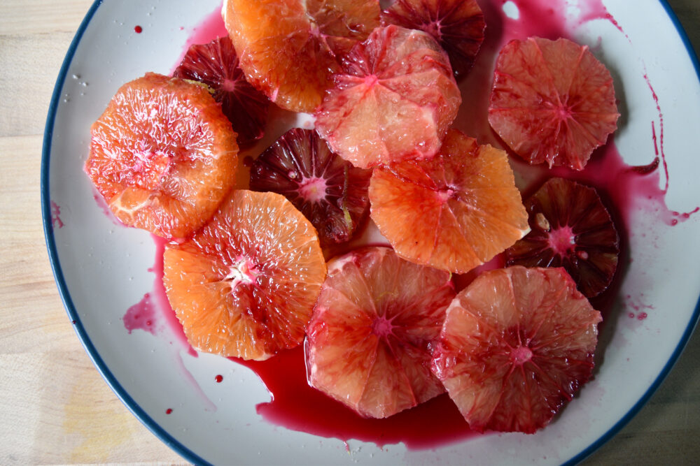 A citrus salad, made of sliced up citrus topped with a red hibiscus syrup