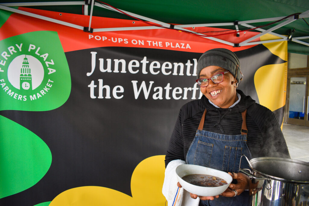 Chef Sarah Germany poses in front of a backdrop that reads "Juneteenth on the Waterfront" at the Foodwise Classroom at the Ferry Plaza Farmers Market in San Francisco.