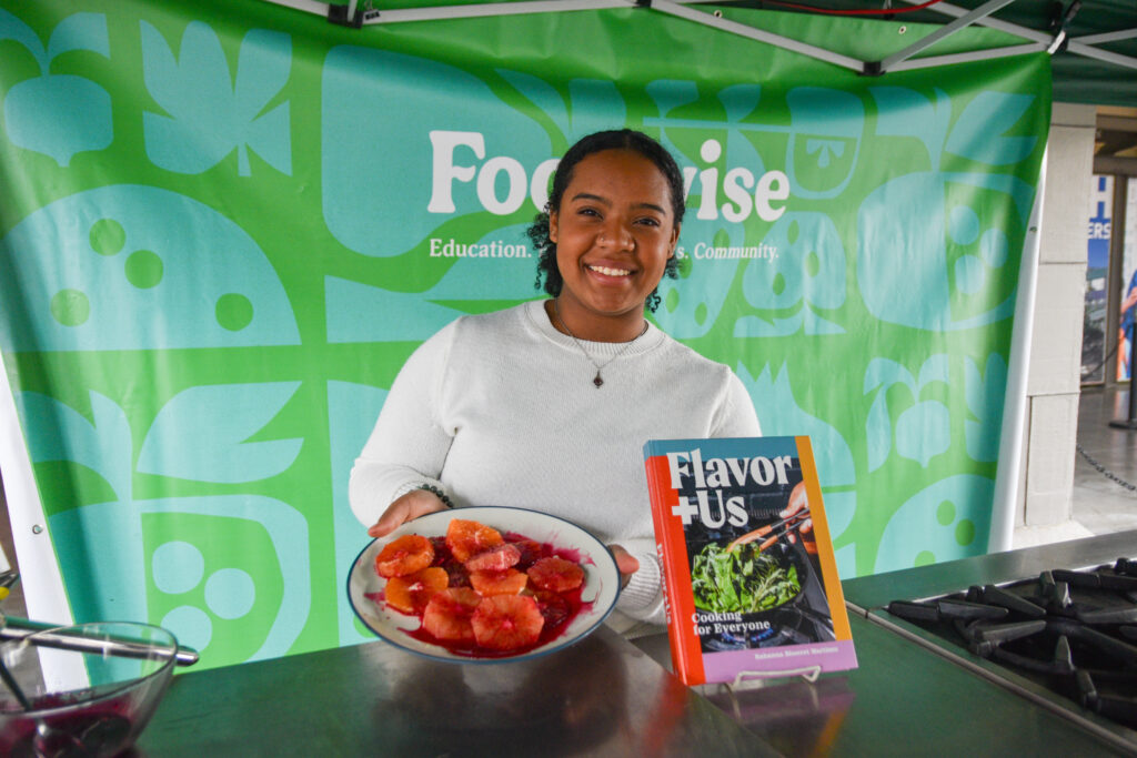 Rahanna Bisseret Martinez poses with a dish of citrus salad and a copy of her book, Flavor + Us at the Foodwise Classroom at the Ferry Plaza Farmers Market in San Francisco.