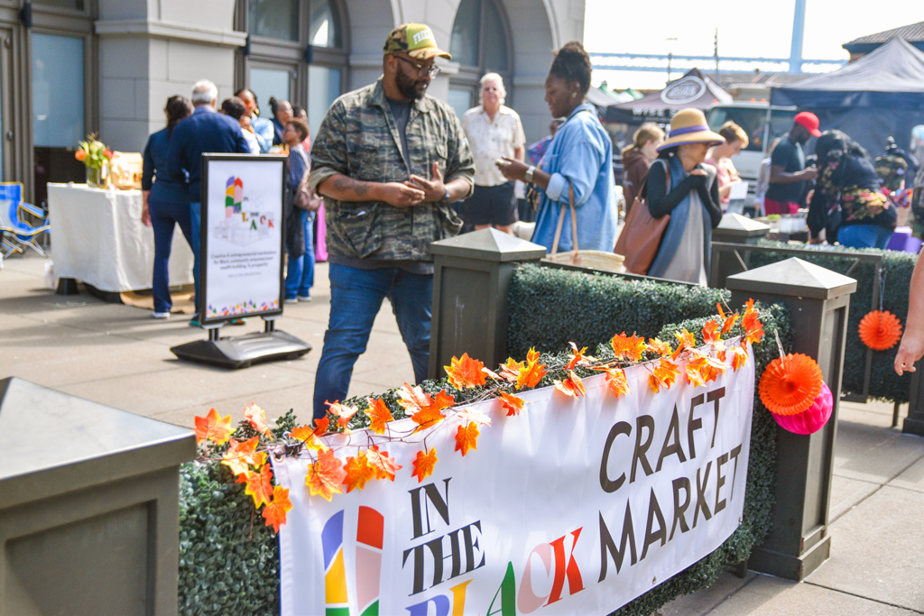 A white banner with In The Black's logo on it that says "Craft Market" at the Ferry Plaza Farmers Market in San Francisco