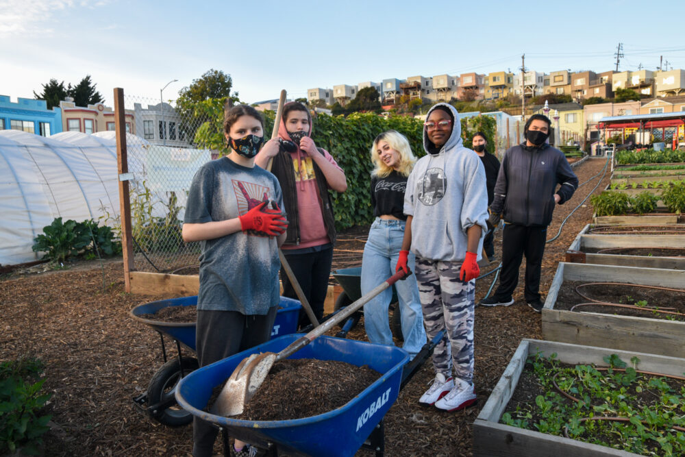 Foodwise Teens pose with a wheelbarrow on a farm.