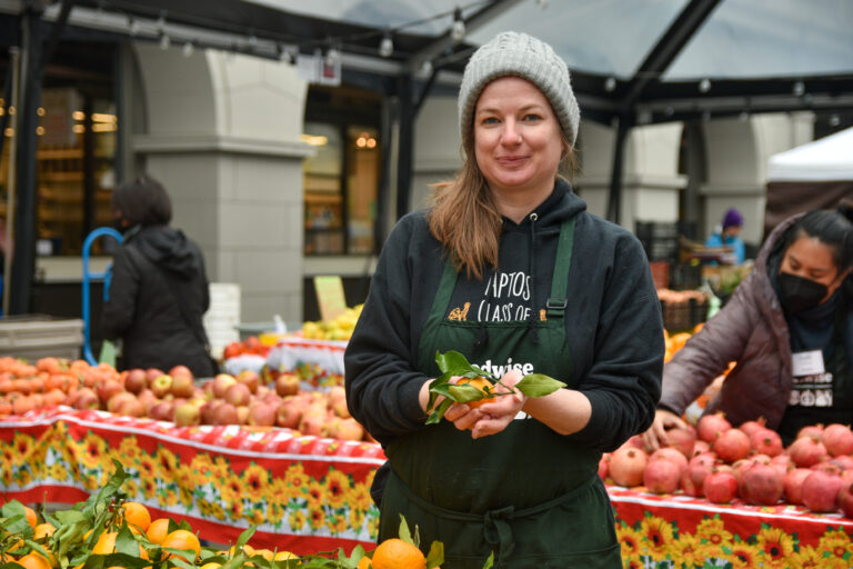 Naomi Webb holds a mandarin orange at the farmers market