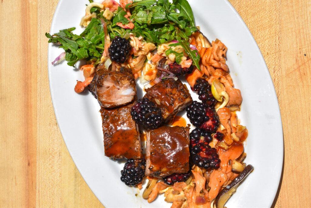 Riblets, served with mushrooms and arugula, on a white dish.