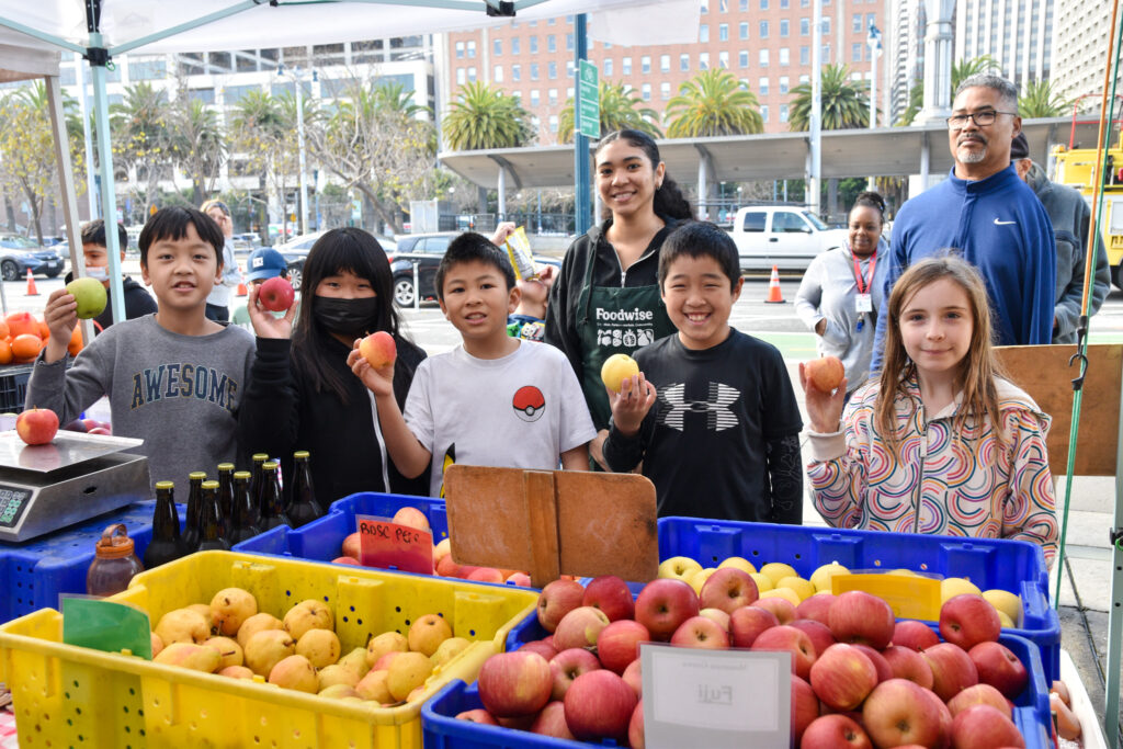 Foodwise intern Erica Tate poses with a group of Foodwise Kids holding apples