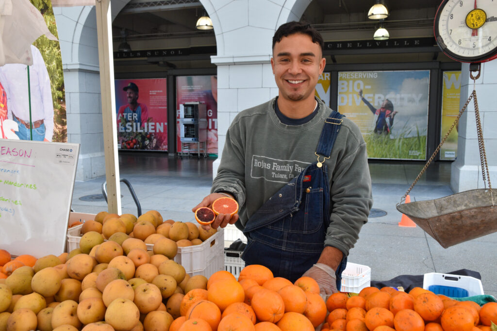 Ramon Rojas holds citrus at Rojas Family Farms' stand at the Ferry Plaza Farmers Market