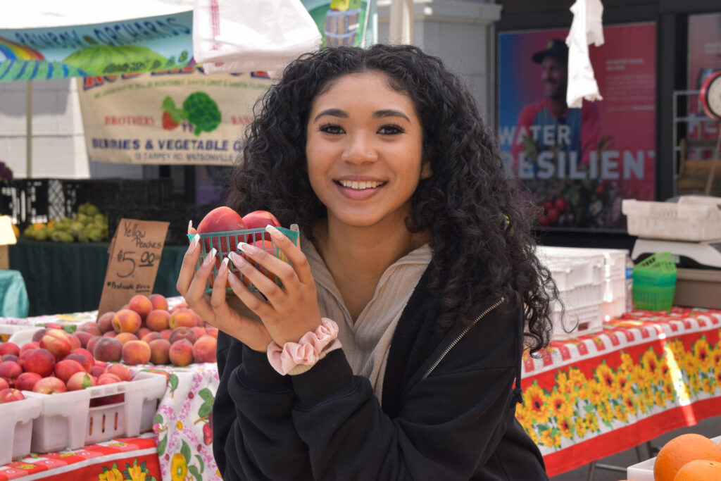 Photo of Foodwise Intern Erica Tate posing with a basket of fruit at the farmers market.
