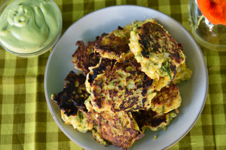 Zucchini cakes served on a ceramic dish, with an avocado cilantro sauce on the side