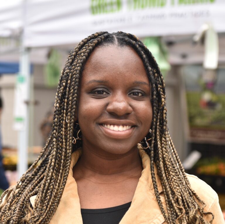 A smiling woman with blonde braids, a beige blazer, and a black shirt.