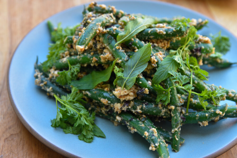 A plate with green beans sprinkled with tofu and garnished with chives, mint, and sisho