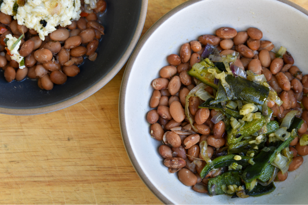 Two bowls of beans, one with a topping of poblano strips, and the other with a topping of ricotta cheese