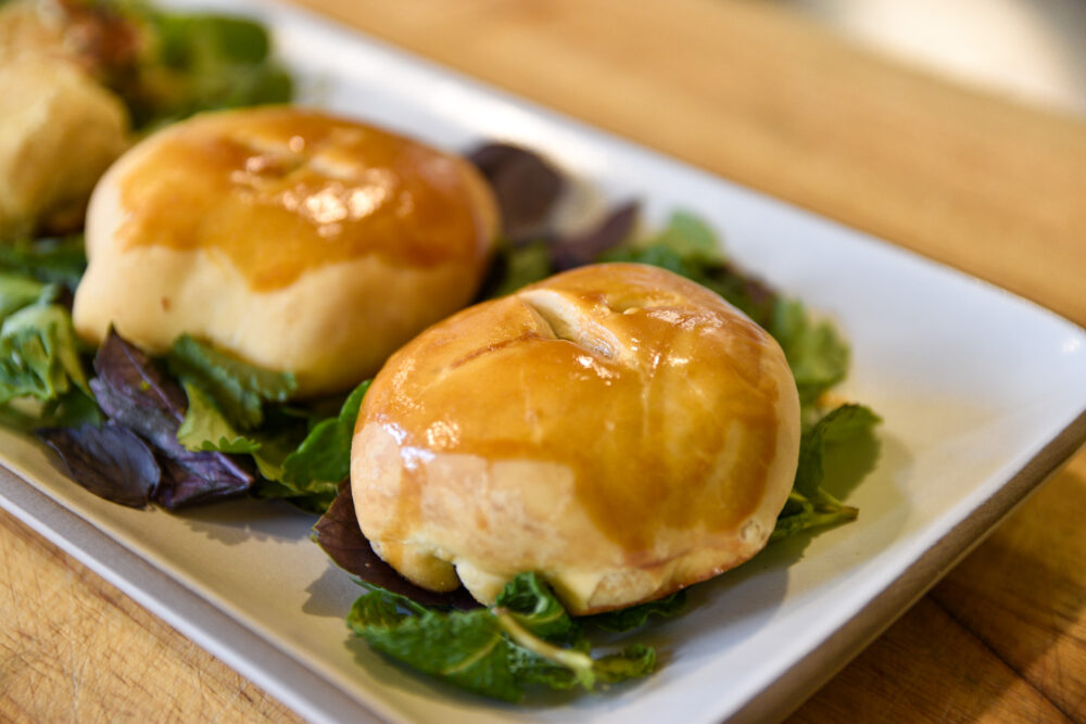 Two wife cakes on a bed of leafy greens, on top of a rectangular, white plate.