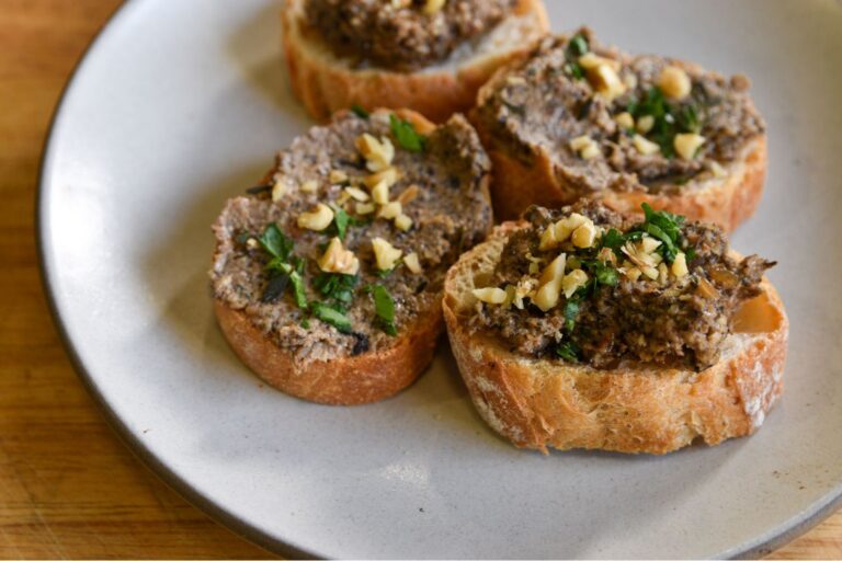 Four small pieces of toast topped with a mushroom pate, walnuts, and chopped parsley.